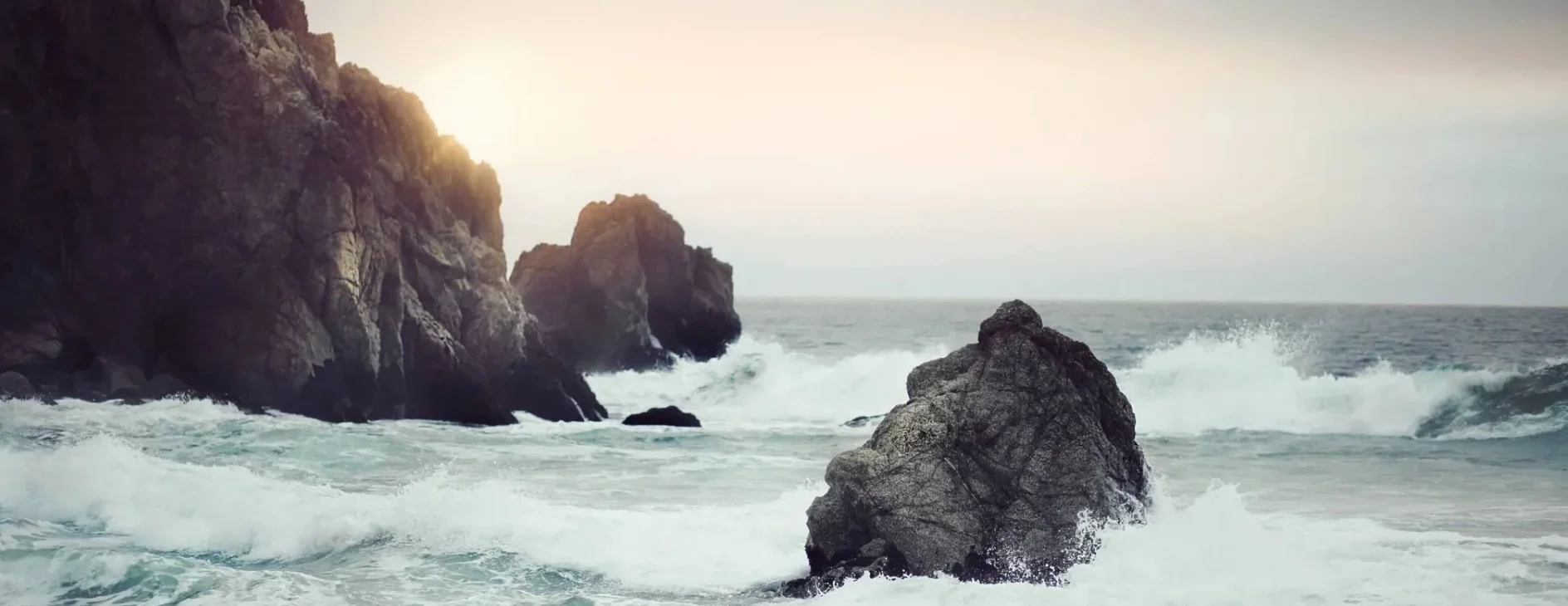 qtq80-fAZcBe A beach with waves crashing on it and rocks in the water.