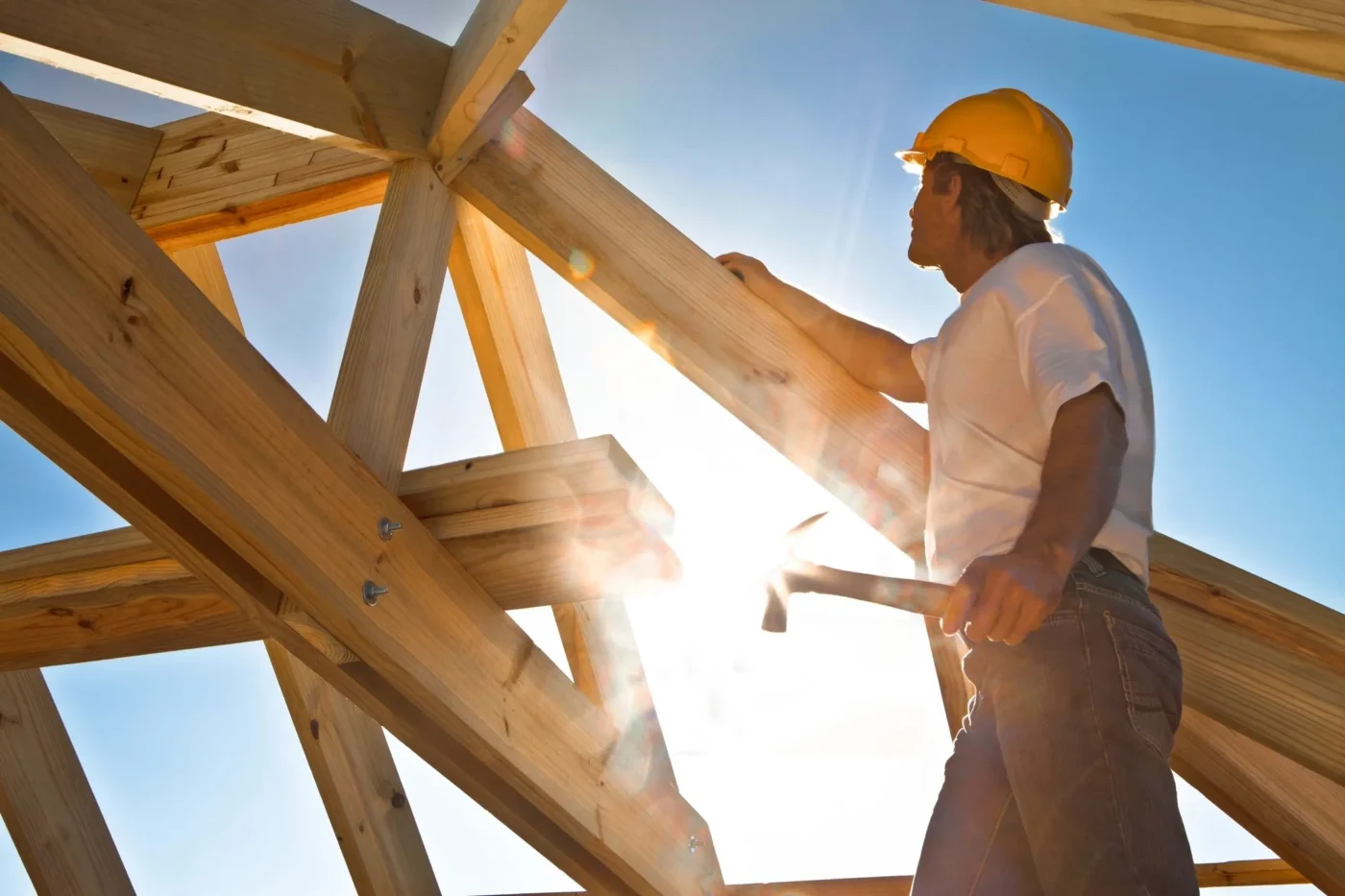 A man in yellow hard hat working on wooden structure.