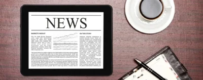 A tablet with news on it sitting next to an open notebook.