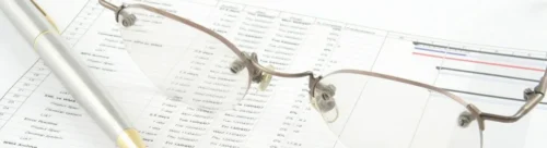 A pen and glasses sitting on top of papers.