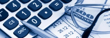 A calculator, pen and glasses on top of some papers.