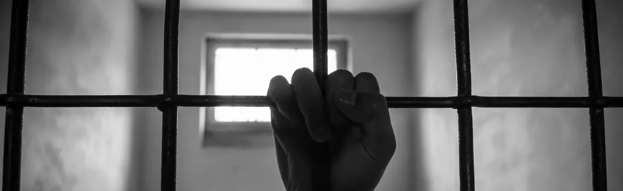 A person 's hand is holding onto bars in a jail cell.