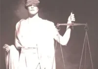 A woman holding a scale and blindfold in front of her face.