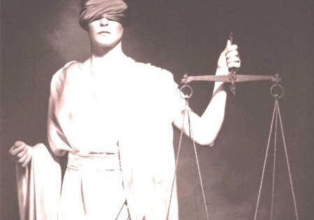 LJ A woman holding a scale and blindfold in front of her face.