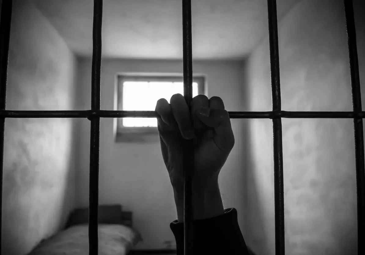 A person 's hand is holding onto bars in a jail cell.