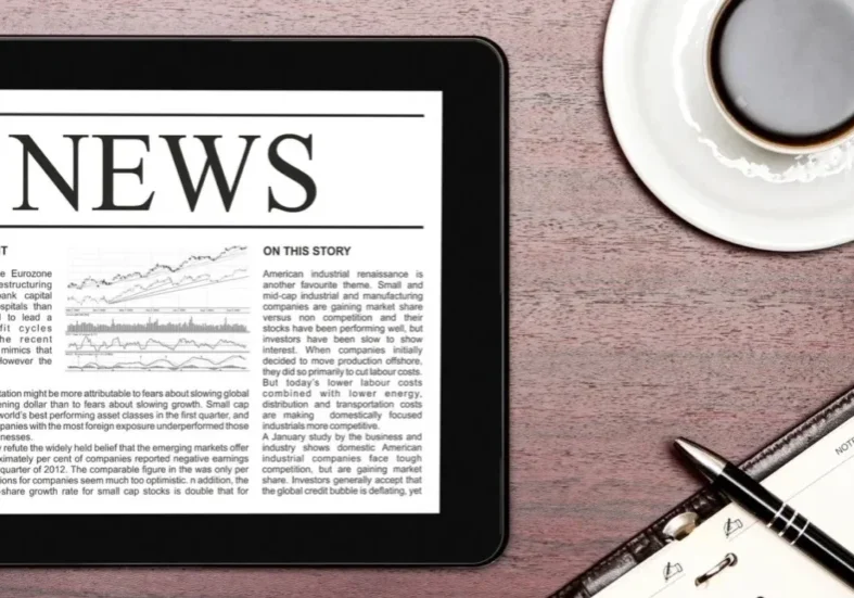 qtq80-JAMmKI A tablet with news on it sitting next to an open notebook.