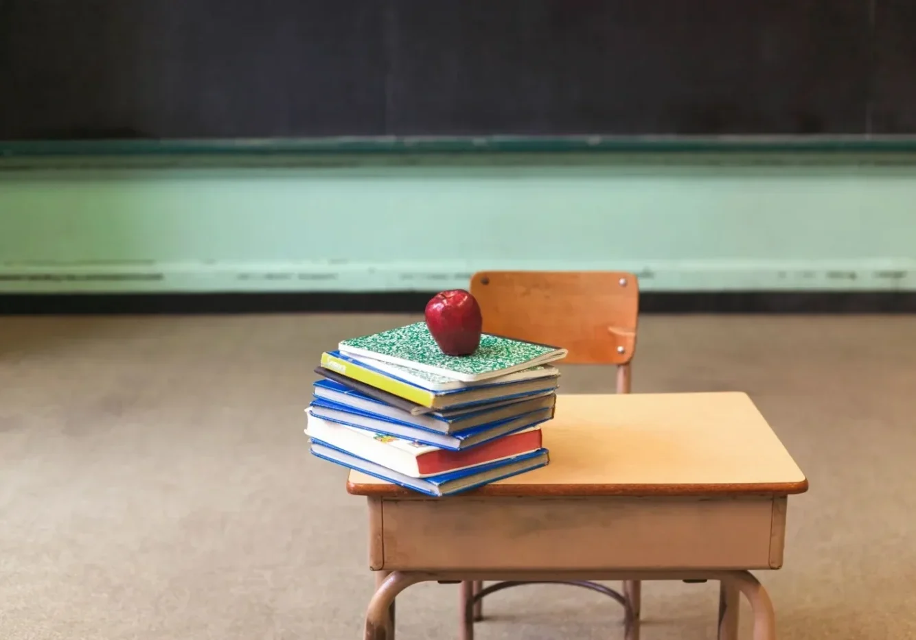 A stack of books and an apple on top of a desk.