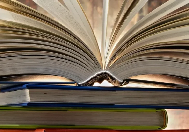 qtq80-swFjIm A book is open on top of some books.
